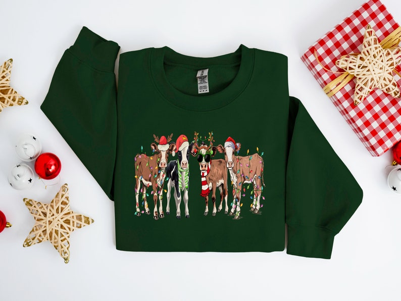 May include: A green Christmas sweater with a design of four cows wearing Santa hats and reindeer antlers. The cows are decorated with Christmas lights.