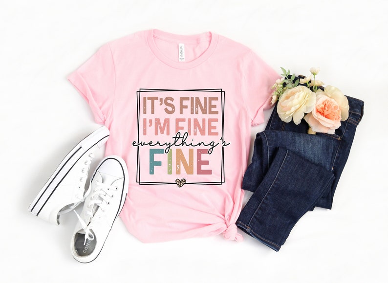 May include: Pink t-shirt with the text "It's fine I'm fine everything's fine" in a colorful, distressed font.