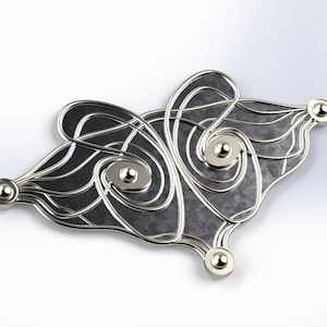 Puede incluir: Broche plateado con un diseño intrincado y fluido. Presenta un centro texturizado gris oscuro y pequeños adornos esféricos. La forma general es orgánica y abstracta, adecuada para añadir un toque único a cualquier atuendo.