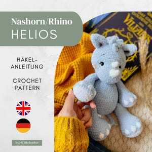 May include: A light blue crochet rhino toy with a soft, fuzzy texture, featuring small ears, a horn, and rounded limbs. The image includes text reading Nashorn/Rhino HELIOS, HÄKEL-ANLEITUNG, CROCHET PATTERN, and the brand name InaMiHäkelzauber.