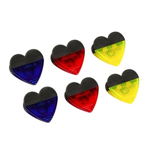 May include: Six heart-shaped clips with black tops and translucent colored bottoms. The colors are red, blue, yellow, and green.