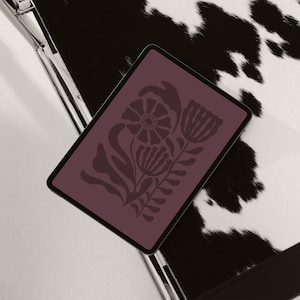 May include: A digital tablet displaying a purple background with a black floral design. The tablet is lying on a black and white surface.