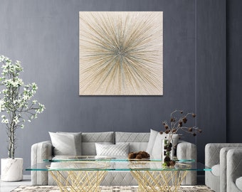 May include: A square abstract painting with a burst of gold and silver lines radiating from the center. The painting is hanging on a gray wall above a gray sofa.