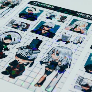 May include: Sticker sheets featuring various anime-style illustrations of characters from the video game "NieR:Automata." The stickers have a holographic finish and are arranged on a grid pattern. The text "NieR: Automata" and "Penguinsbite" are visible.