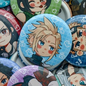 May include: A collection of colorful, round pinback buttons featuring anime-style character illustrations. The buttons have various background colors, including blue, green, and red, and depict different characters with detailed facial features and hairstyles.