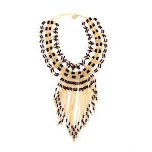 May include: A cream-colored beaded necklace with a geometric design. The necklace features a series of square and circular patterns in cream and dark brown beads. The bottom portion has cream-colored beaded fringe.