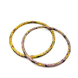 May include: Two thin, colorful bangles. One is yellow with green and brown accents, the other is pink with yellow and black accents. The bangles are circular and appear to be made of a lightweight material.