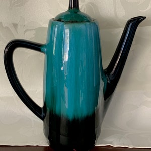 May include: A teal and black ceramic teapot with a lid. The teapot has a rounded body and a spout on the side. The handle is black.