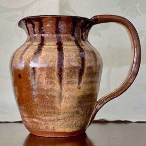 May include: A brown and tan ceramic jug with a wide mouth and a handle. The jug has vertical brown stripes and a glazed finish.