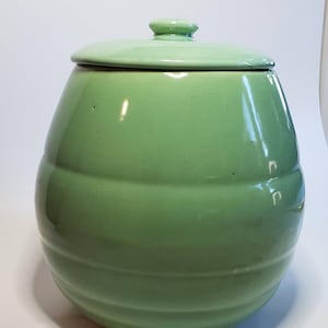 May include: A green ceramic cookie jar with a lid and a rounded, ribbed body.