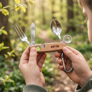 May include: A multi-tool camping utensil set with a light wood handle featuring the name ANTON. The tool includes a stainless steel fork, knife, and spoon, along with a small circular spirit level and a magnifying glass, plus a metal carabiner.