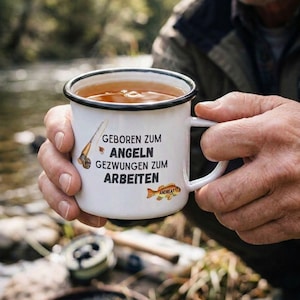 Può includere: Tazza smaltata bianca con bordo nero, piena di una bevanda calda. La tazza presenta il testo "GEBOREN ZUM ANGELN GEZWUNGEN ZUM ARBEITEN" e una grafica di pesce. La tazza è tenuta da una persona.