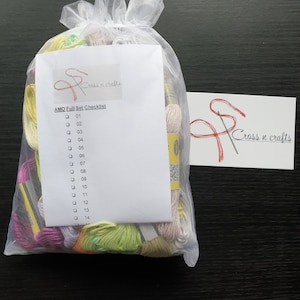 Puede incluir: Una bolsa de malla blanca llena de hilo de bordar de colores. La bolsa tiene una lista de verificación adjunta con el texto "AMO Full Set Checklist" y los números del 01 al 14.