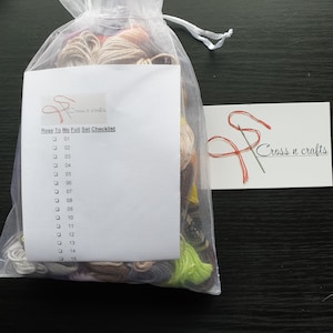 May include: A white mesh bag filled with colourful embroidery floss, a checklist for a cross stitch project titled "Rose To Me Full Set Checklist" with numbers 01-15, and a small card with the text "Cross n crafts".