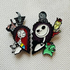 Könnte beinhalten: Zwei Emaille-Pins mit Figuren aus Nightmare Before Christmas. Der linke Pin zeigt Sally mit roten Haaren und einem blau-gelben Kleid. Der rechte Pin zeigt Jack Skellington mit einem schwarz-weiß gestreiften Anzug und einem violetten Hintergrund.