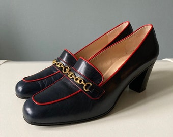 May include: A pair of navy blue leather heeled shoes with a red trim and a gold chain detail.