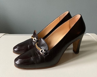 May include: A pair of brown leather heeled shoes with a gold chain detail and silver buckles.