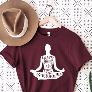 May include: Burgundy t-shirt with a white silhouette of a person in a yoga pose. The text "every thing you need is within me" is printed on the shirt.