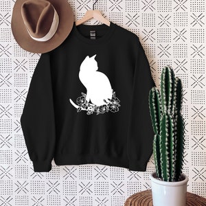 May include: Black sweatshirt with a white silhouette of a cat sitting in a floral arrangement.