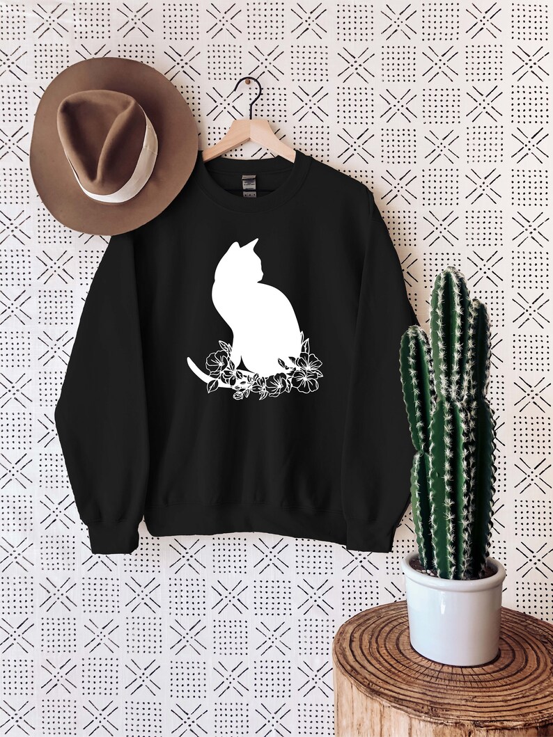 May include: Black sweatshirt with a white silhouette of a cat sitting in a floral arrangement.