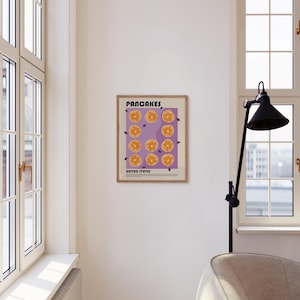 May include: A framed wall art print featuring a purple background with a grid of twelve illustrated golden-brown pancakes. The text at the top reads PANCAKES and the text at the bottom reads UNITED STATES, followed by a small paragraph of text.