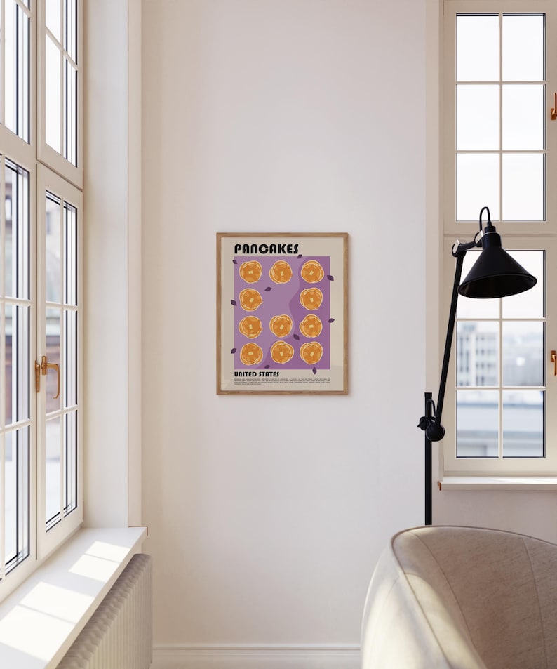 May include: A framed wall art print featuring a purple background with a grid of twelve illustrated golden-brown pancakes. The text at the top reads PANCAKES and the text at the bottom reads UNITED STATES, followed by a small paragraph of text.