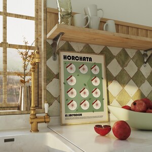 May include: A rectangular wall poster in a light wood frame featuring the text HORCHATA and EL SALVADOR. The poster displays a grid of twelve circular illustrations of sliced horchata ingredients on a sage green background with small leaves.