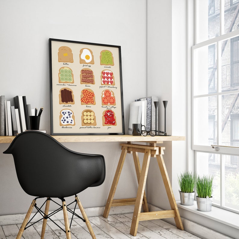 May include: A framed illustration of 12 different toast toppings, including butter, fried egg, avocado, cucumber and banana, bacon, yogurt and strawberry, chocolate, beans, tomato and cottage cheese, blueberries, peanut butter and banana, and jam. The illustration is on a white background and is framed in a black frame. The frame is hanging on a white wall.