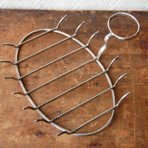 May include: A silver metal dish rack with a circular handle. The rack has eight hooks and is designed to hold dishes or other items.