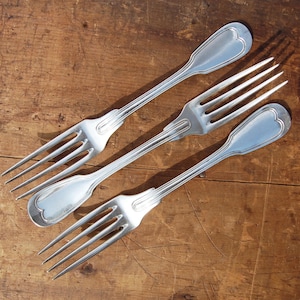 Puede incluir: Tres tenedores de plata con mangos ornamentados, dispuestos sobre una superficie de madera.