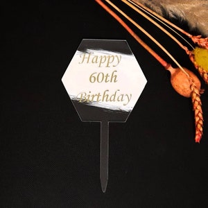 以下が含まれることがあります： 「Happy 60th Birthday」と金色で書かれた黒と白の六角形のケーキトッパーです。