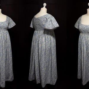 Op de afbeelding: Een witte jurk met een blauw bloemenpatroon. De jurk heeft een getailleerd lijfje met een vierkante halslijn en een volle rok. De mouwen zijn kort en zwierig.