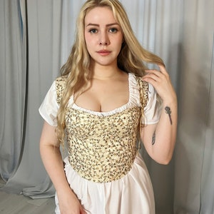 May include: A white dress with a cream-colored embroidered bodice. The bodice has a sweetheart neckline and a fitted silhouette.