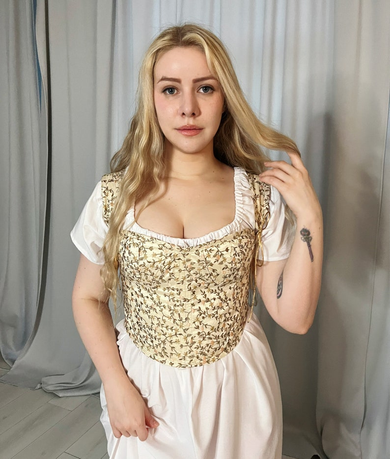 May include: A white dress with a cream-colored embroidered bodice. The bodice has a sweetheart neckline and a fitted silhouette.