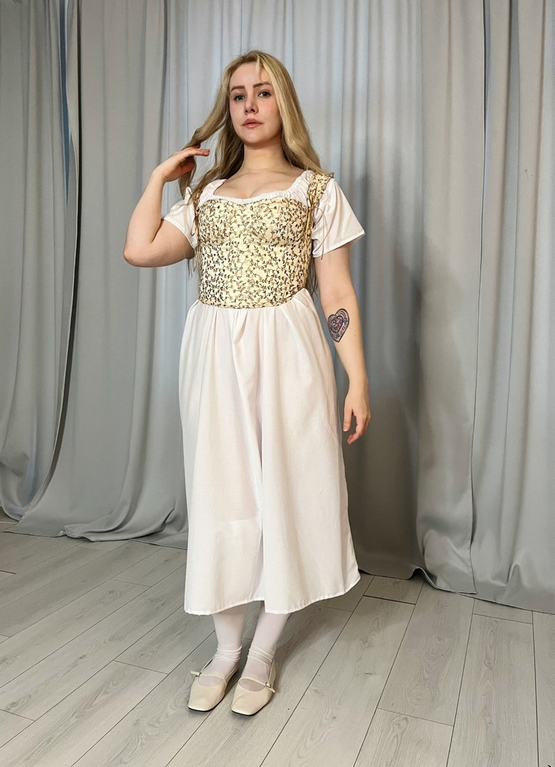May include: A white dress with a gold embroidered bodice and short sleeves. The dress is worn by a person with long blonde hair and white shoes.