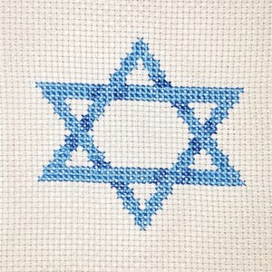 May include: Framed cross-stitch art featuring a blue Star of David on a cream-colored background. The artwork is enclosed in a black wooden frame, creating a simple yet elegant presentation. Ideal for home decor.