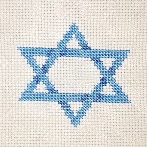 May include: A framed cross-stitch of a blue Star of David on a white background.