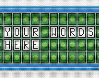May include: A cross-stitch pattern featuring a rectangular game board with a blue and grey border. The board contains a grid of green squares, with white tiles displaying the black text "YOUR WORDS HERE" in the center of the design.