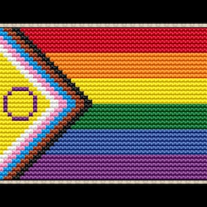 Puede incluir: Una bandera del orgullo con un triángulo negro, marrón, azul claro, rosa y blanco en la esquina superior izquierda. El triángulo contiene un círculo amarillo con un círculo morado en su interior. El resto de la bandera es un arcoíris con rayas rojas, naranjas, amarillas, verdes, azules, índigo y violetas.