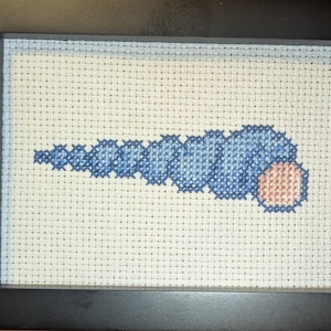 May include: Cross-stitch artwork in a black frame. The design features a blue and peach-coloured pattern on a white background. The pattern resembles a stylised worm or caterpillar. The frame is rectangular.