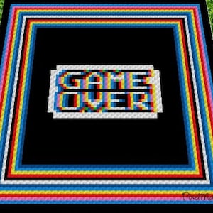 May include: A colorful crochet blanket with a black background and the words "GAME OVER" in pixelated letters. The blanket has a multi-colored border with stripes of pink, blue, yellow, red, and white.