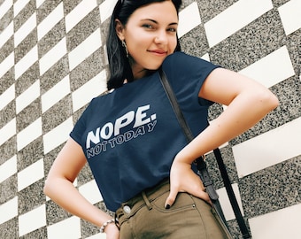 May include: A woman wearing a navy blue t-shirt with the text "NOPE. NOT TODAY" in white. She is wearing olive green pants and has a black crossbody bag.