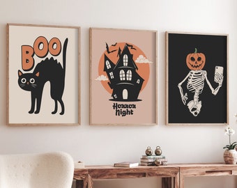 May include: Three Halloween-themed prints with black frames. The first print features a black cat with the word "BOO" above it. The second print features a black silhouette of a house with the words "Horror Night" below it. The third print features a skeleton with a pumpkin head taking a selfie.