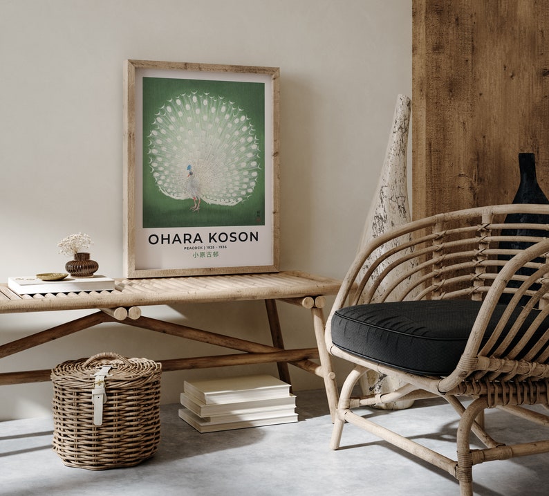 May include: A framed print of a white peacock with its tail feathers spread out. The print is on a green background and has the text "OHARA KOSON" and "PEACOCK (1945 - 1936)" in black text. The print is hanging on a white wall above a wooden bench with a wicker basket and books.