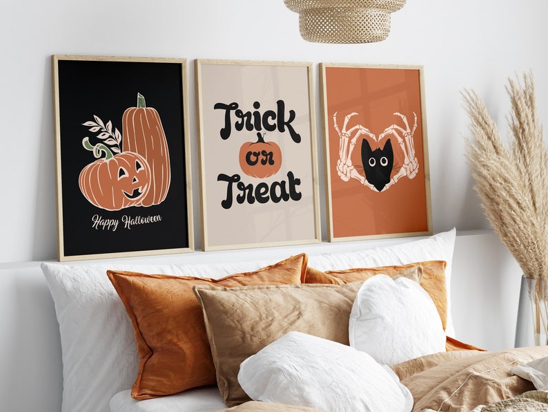 May include: Three framed Halloween-themed art prints. The first features pumpkins and the text "Happy Halloween." The second says "Trick or Treat." The third shows a black cat within a heart made of skeleton hands. The prints have a neutral color palette.