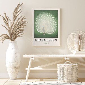 May include: A vintage poster featuring a white peacock with its tail feathers spread out. The poster has a green background and the artist's name, "Ohara Koson", is printed at the bottom. The text "Peacock 1923 - 1936" and "小原古邨" are also printed on the poster.