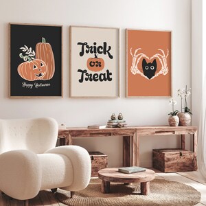 May include: Three framed Halloween-themed art prints. The first features orange pumpkins on a black background with the text "Happy Halloween." The second says "Trick or Treat" with a pumpkin. The third shows a black cat in a heart made of skeleton hands on an orange background.