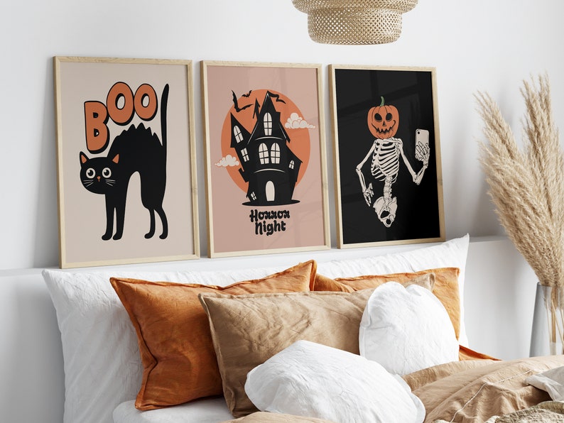 May include: Three Halloween-themed prints in wooden frames. The first print features a black cat with the word "BOO" above it. The second print features a silhouette of a haunted house with the text "Halloween Night". The third print features a skeleton with a pumpkin head taking a selfie.