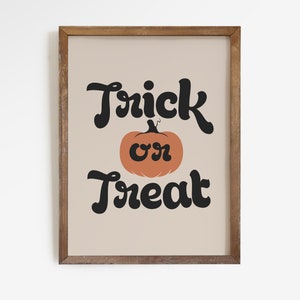 May include: A framed print with the words "Trick or Treat" in black script above and below an orange pumpkin illustration. The background is a light beige color, and the frame is made of wood.