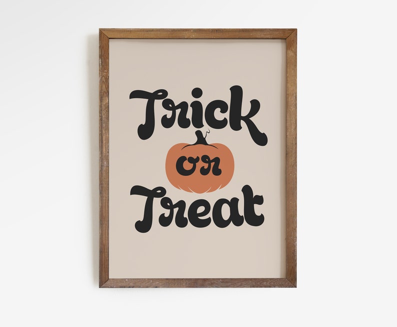 May include: A framed print with the words "Trick or Treat" in black script above and below an orange pumpkin illustration. The background is a light beige color, and the frame is made of wood.